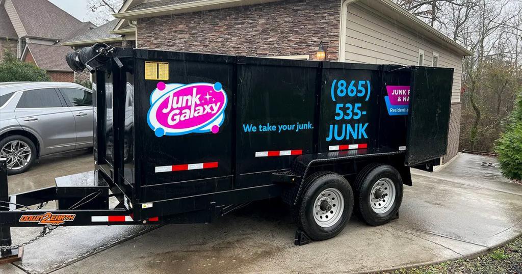 junk-galaxy-knoxville-black-professional-grade-junk-removal-trailer-with-dual-axles-vibrant-galaxy-branding-in-blue-and-pink-parked-on-a-residential-concrete-driveway