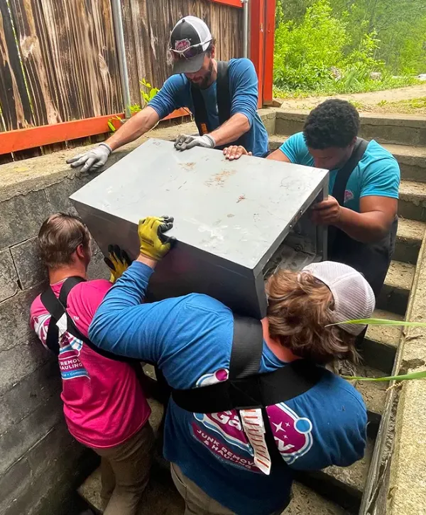 Junk Galaxy workers moving a large appliance out of a confined space during a hoarder cleanout project