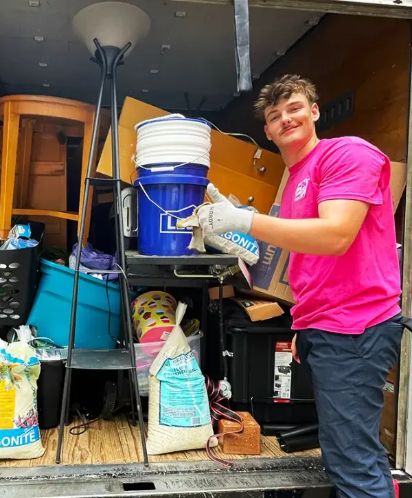 a Junk Galaxy worker posing with a truck full of unwanted items and furniture during a home cleanout project