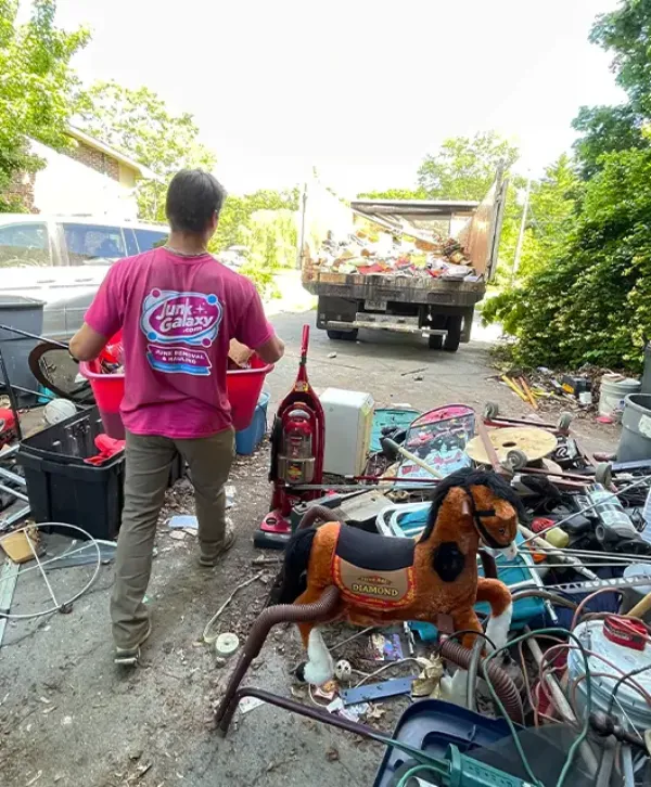 a person working for Junk Galaxy loading items into a truck in an outdoor area cluttered with various unwanted items