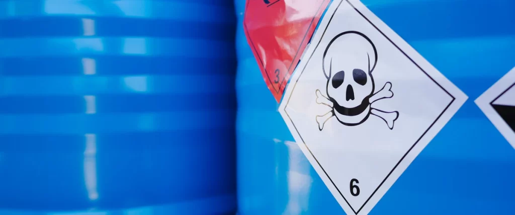 Close-up of blue industrial barrels featuring a toxic skull and crossbones warning label used for storing hazardous materials.