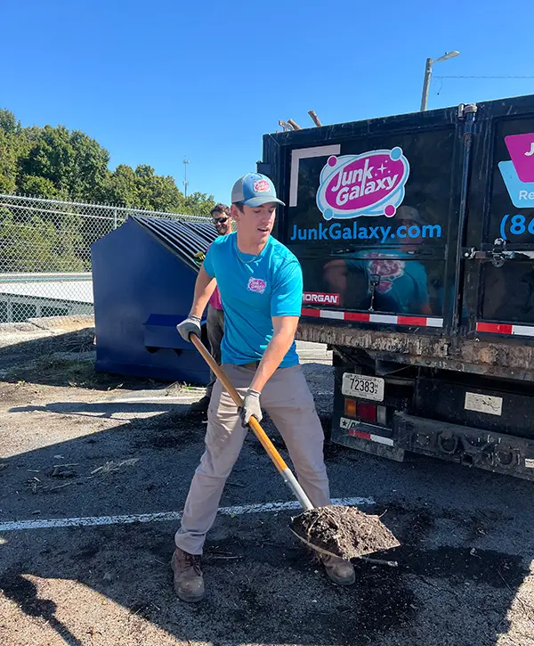 Junk removal worker cleaning debris beside hauling truck during commercial cleanup service